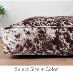May include: A brown and white cowhide dog bed with a stitched seam around the edge.