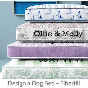 May include: A stack of dog beds with various patterns and colors. The top bed has a blue and white sailboat design. The second bed has the text "Ollie & Molly". The third bed is purple. The bottom bed has the text "WALTER".