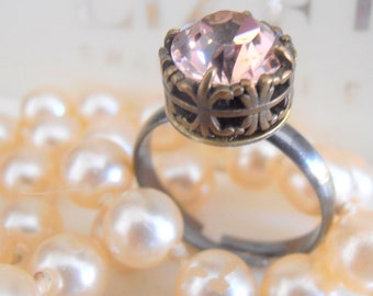 May include: A delicate ring with a pink crystal set in a gold-toned crown-shaped setting. The ring is on a bed of white pearls.