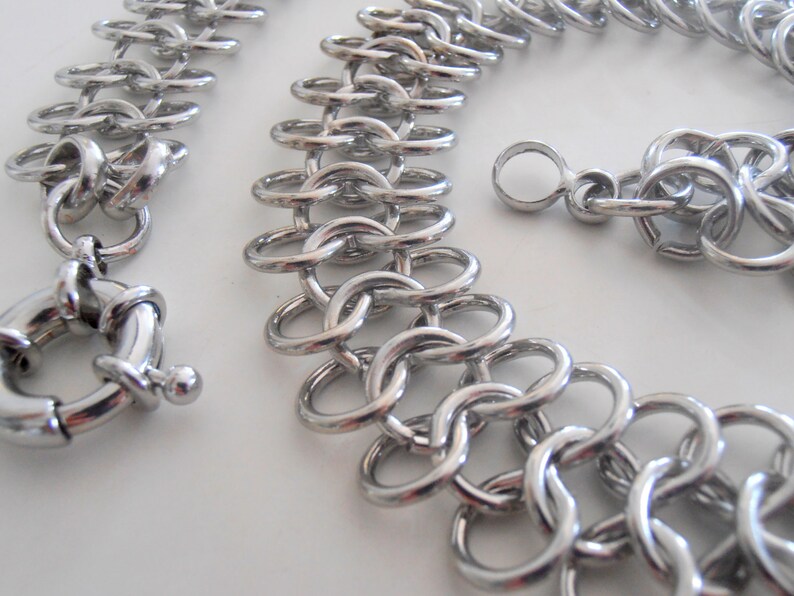 May include: A silver chain necklace with a large, round clasp. The chain is made of interlocking metal rings.