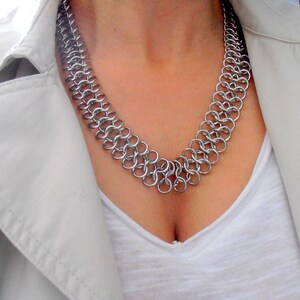 May include: A silver chainmail necklace with a delicate, intricate design. The necklace is made of small, interconnected metal rings.