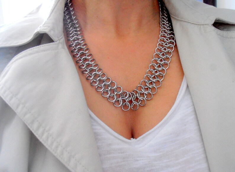 May include: A silver chainmail necklace with a delicate, intricate design. The necklace is made of small, interconnected metal rings.
