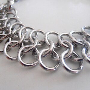 May include: A silver chain bracelet with a unique interlocking design. The bracelet is made of multiple small, linked circles.