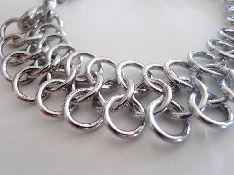 May include: A silver chain bracelet with a unique interlocking design. The bracelet is made of multiple small, linked circles.