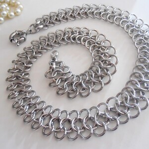 May include: A silver chain necklace and bracelet set with a double chain link design.