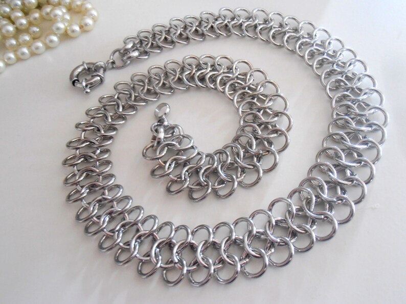 May include: A silver chain necklace and bracelet set with a double chain link design.