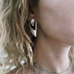 May include: A pair of silver geometric earrings with a sharp, angular design. The earrings are made of metal and have a modern, minimalist aesthetic.
