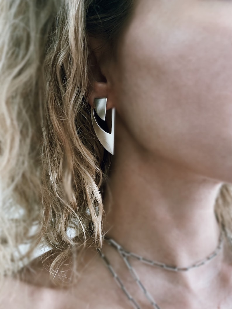 May include: A pair of silver geometric earrings with a sharp, angular design. The earrings are made of metal and have a modern, minimalist aesthetic.