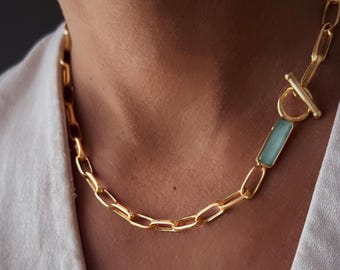 May include: A gold-toned chain necklace featuring elongated oval links and a toggle clasp closure. The necklace includes a rectangular, light blue, semi-translucent stone accent positioned near the toggle mechanism.