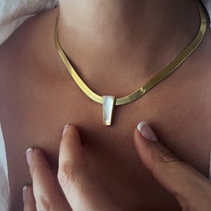 Puede incluir: Un collar de cadena dorada con un colgante rectangular blanco.
