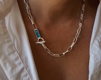 May include: A silver chain necklace with a turquoise stone toggle clasp.