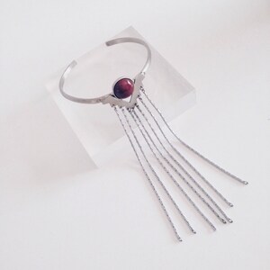 May include: A silver bracelet with a red stone and a fringe of silver chains.