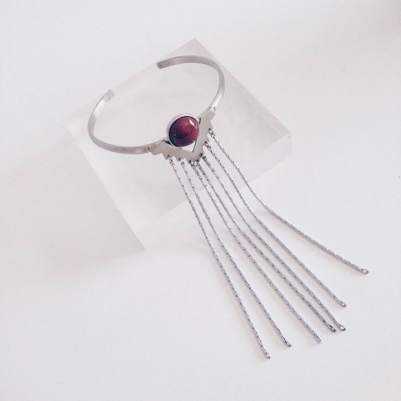 May include: A silver bracelet with a red stone and a fringe of silver chains.