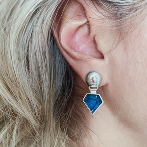 Puede incluir: Pendientes de plata con una piedra preciosa azul en forma de diamante y una bola de plata en la parte superior.