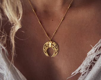 May include: A gold necklace with a delicate chain and a large, ornate crescent moon pendant.