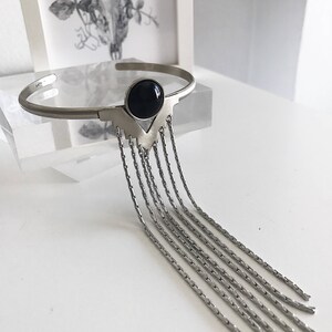 May include: A silver bracelet with a black gemstone and a fringe of dangling chains.
