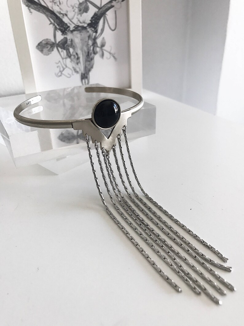May include: A silver bracelet with a black gemstone and a fringe of dangling chains.