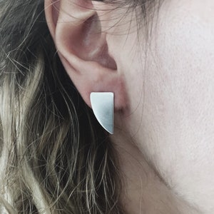 May include: A pair of silver geometric earrings with a triangular shape. The earrings are simple and modern in design.