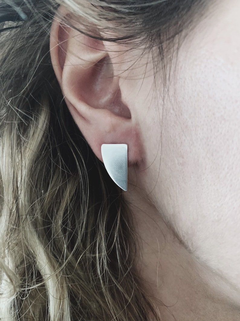 May include: A pair of silver geometric earrings with a triangular shape. The earrings are simple and modern in design.
