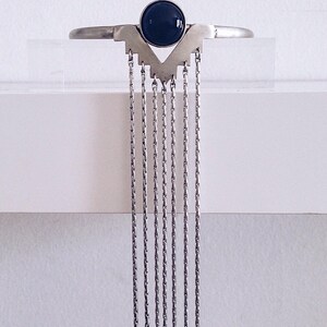 May include: A silver necklace with a black gemstone pendant and multiple dangling chains.