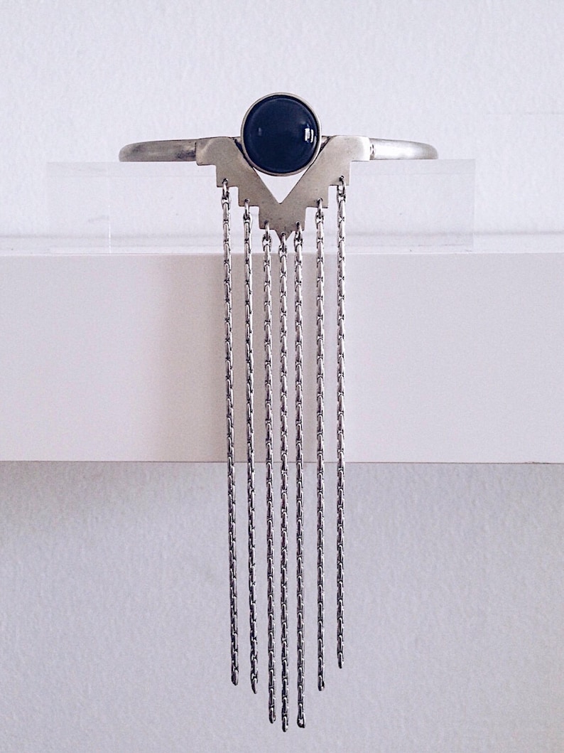 May include: A silver necklace with a black gemstone pendant and multiple dangling chains.