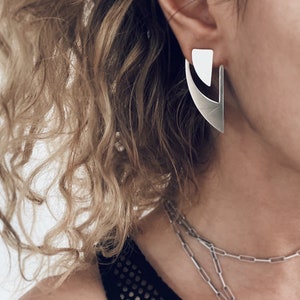 May include: Silver geometric earrings with a triangular shape. The earrings are dangling and have a modern design.