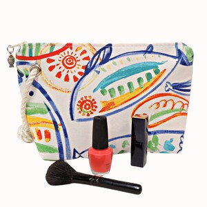 May include: A white canvas makeup bag with a colorful fish design. The bag has a drawstring closure and a rope handle. The bag is filled with makeup brushes, nail polish, and lipstick.