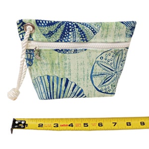 Monedero náutico de pulsera, conchas azules sobre fondo verde, forrado con lona.
