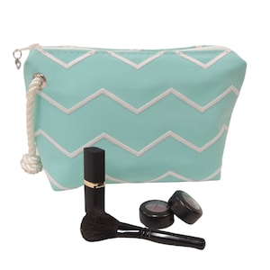 May include: A light blue zippered makeup bag with a white chevron pattern. The bag is open and there are two small round makeup containers and a lipstick inside.