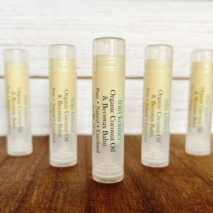 Pu&ograve; includere: Cinque tubetti di balsamo per le labbra sono disposti su una superficie di legno. Ogni tubetto ha un tappo trasparente e un'etichetta con il testo "fr&aring;n kr&auml;mer Organic Coconut Oil & Beeswax Balm". Il balsamo all'interno &egrave; di colore giallo chiaro.