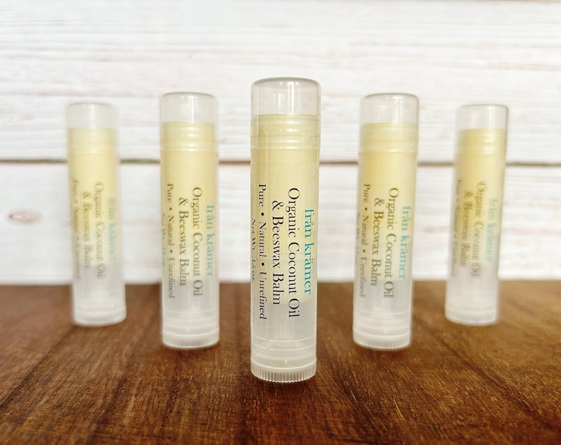 Pu&ograve; includere: Cinque tubetti di balsamo per le labbra sono disposti su una superficie di legno. Ogni tubetto ha un tappo trasparente e un'etichetta con il testo "fr&aring;n kr&auml;mer Organic Coconut Oil & Beeswax Balm". Il balsamo all'interno &egrave; di colore giallo chiaro.