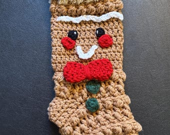 May include: A handmade Christmas stocking in the shape of a gingerbread man. The stocking is crocheted in shades of brown, with a fluffy tan top. It features a red bow tie, green buttons, and a white smile.