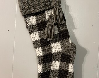 May include: A handmade Christmas stocking with a gray, black, and white buffalo plaid pattern. The top cuff and hanging loop are solid gray. Two gray tassels hang from the side.