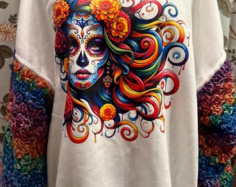 May include: White sweatshirt featuring a vibrant sugar skull design with colorful floral accents and rainbow hair. The sleeves are adorned with a textured, rainbow-colored crochet pattern. A unique and artistic apparel item.