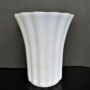 May include: A white ceramic vase with a fluted design. The vase has a wide mouth and a narrow base.