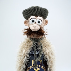 Op de afbeelding: Een gehaakte flesstopper in de vorm van een man met een groene hoed, bruine snor en een witte bontjas. De flesstopper zit op een fles St. Hubertus likeur met een gouden etiket.