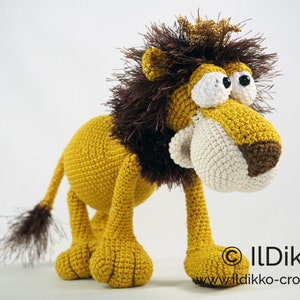 May include: A crocheted lion with a brown mane, a gold crown, and large white eyes. The lion is standing on a white surface.