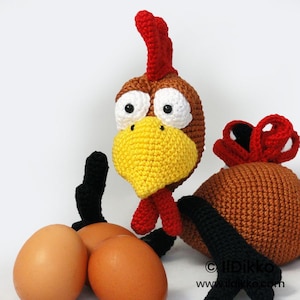 May include: A handmade crochet chicken with a red comb, wattle, and beak. The chicken has large white eyes and is brown and yellow. Three brown eggs are in front of the chicken. The chicken is a whimsical, handmade item.