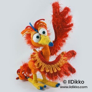 May include: A crocheted bird figure with bright orange and red fuzzy yarn, large white eyes with black pupils, a yellow beak with a blue tip, and a blue crest. The figure has a ruffled collar and text reading &copy; Ildikko www.ildikko.com.