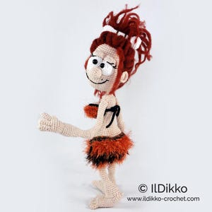 May include: A handmade crochet doll of a cartoon character with red hair and a playful expression. The doll wears a small, furry orange and brown skirt and a matching top. The doll is approximately 25 cm tall.