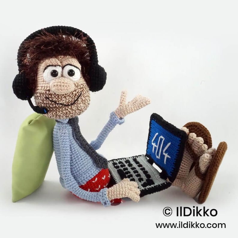 May include: A crocheted doll featuring a brown-haired figure wearing black headphones, a light blue shirt, a dark tie, and red patterned shorts. The figure sits with a crocheted laptop displaying the text 404 on a blue screen. Text reads IIDikko.