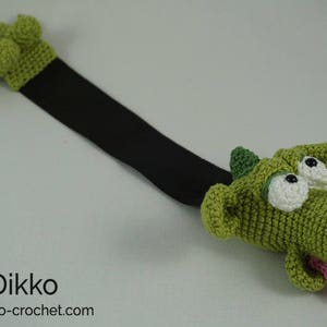 May include: Green crocheted dragon bookmark with a black ribbon. The dragon has large white eyes and a pink tongue sticking out.