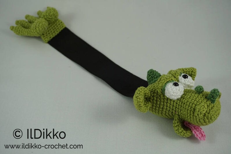May include: Green crocheted dragon bookmark with a black ribbon. The dragon has large white eyes and a pink tongue sticking out.