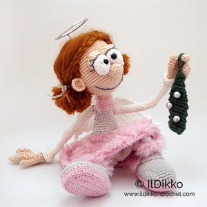 May include: A crocheted doll with auburn hair, a silver halo, and white wings, wearing a pink fuzzy skirt and grey shoes. The doll holds a small dark green crocheted mistletoe ornament with three white beads. Text reads ILDikko www.ildikko-crochet.com.