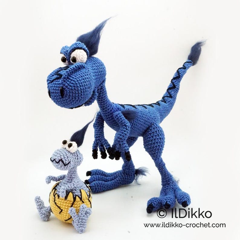 May include: A large blue crocheted dinosaur with black claws and a tuft of blue hair stands next to a smaller light blue crocheted dinosaur emerging from a yellow cracked egg. The text "IlDikko www.ildikko-crochet.com" is visible at the bottom.
