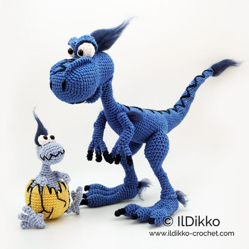 May include: A blue crocheted dinosaur toy with black claws and a tuft of dark blue hair, standing next to a smaller light blue crocheted dinosaur emerging from a yellow cracked egg. The text ILDikko and www.ildikko-crochet.com is visible.