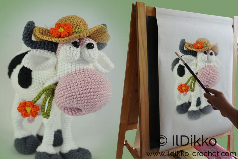 May include: A crocheted cow wearing a brown and orange hat with a flower. The cow is holding a green stem with an orange flower. The cow is standing on a white surface.