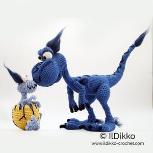 May include: A large blue crocheted dinosaur with dark blue tufts and black claws standing next to a smaller light blue crocheted baby dinosaur emerging from a yellow and black cracked egg. The text ILDikko www.ildikko-crochet.com is visible.