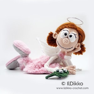 May include: A crocheted doll with auburn hair, a silver halo, and white wings. The doll wears a pink fuzzy skirt, grey and pink shoes, and holds a green leaf with three silver beads. Text reads: ILDikko www.ildikko-crochet.com.