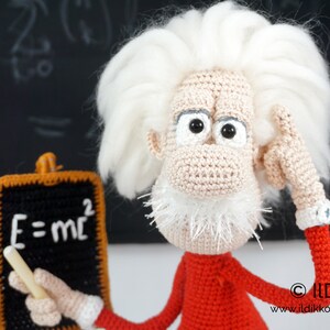 Puede incluir: Mu&ntilde;eco de ganchillo hecho a mano de Albert Einstein, con pelo blanco y un su&eacute;ter rojo. El mu&ntilde;eco sostiene una peque&ntilde;a pizarra con la ecuaci&oacute;n E=mc&sup2;. Un art&iacute;culo &uacute;nico y hecho a mano.